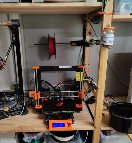 Ein 3D Drucker in Schwarz und Orange steht in einem Regal 